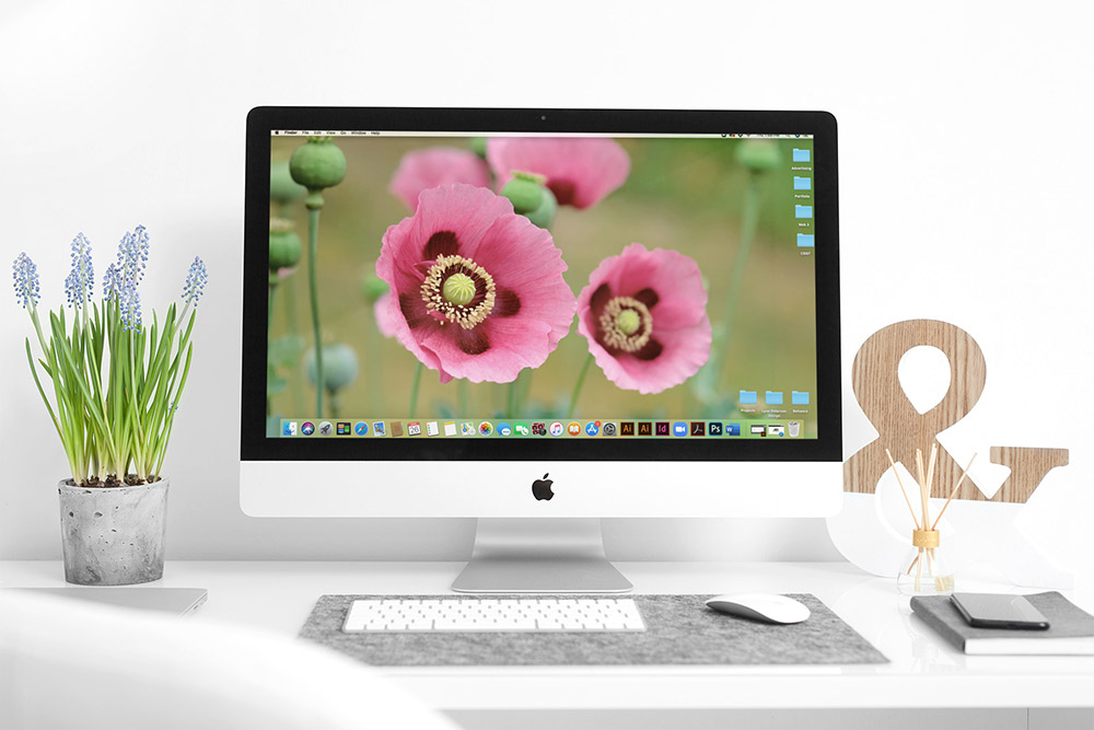 An iMac desktop computer with flowers on the desk