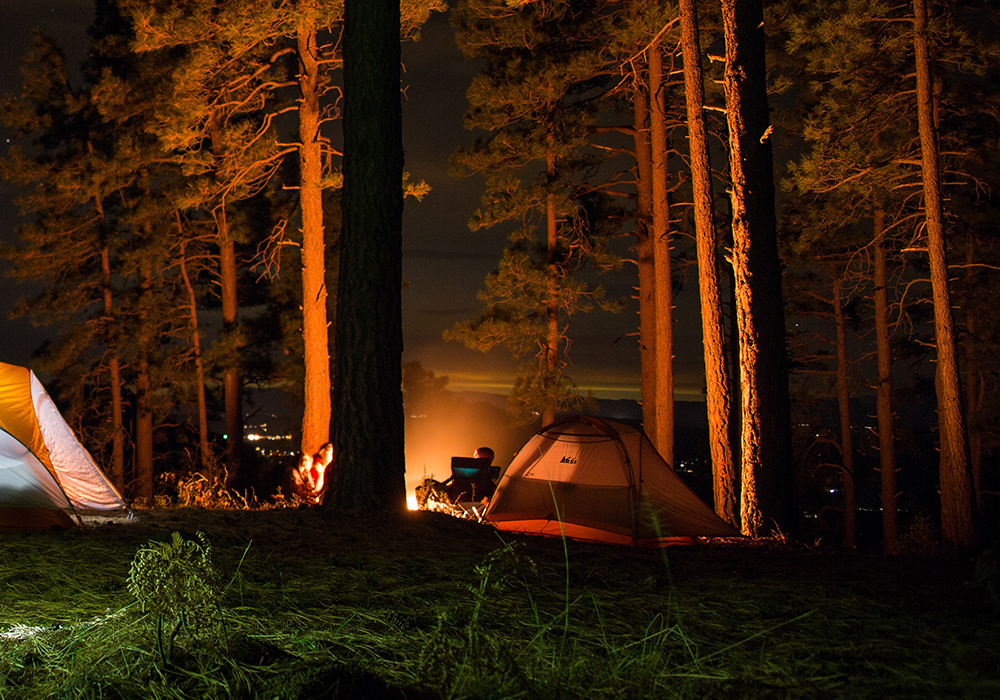 Several tents lit up in the night gathered around a campfire