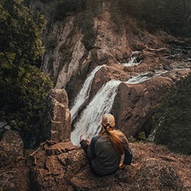 A woman sitting on rocks looking at a waterfall